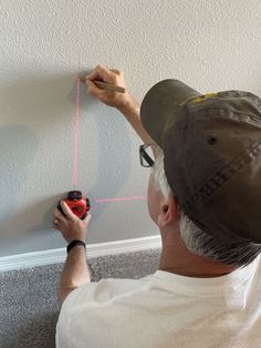 a man is measuring the height of a wall with tape and a screwdriver