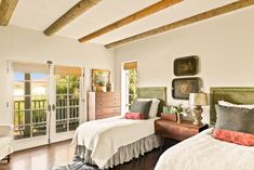 two beds in a room with wooden floors and white walls, along with windows that look out onto the outdoors