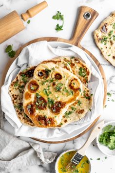 two flatbreads with cheese and herbs on a white plate next to some dipping sauce