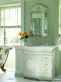 a bathroom with green walls and white furniture in the corner, along with flowers on the counter