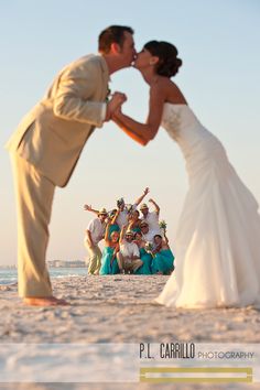 a bride and groom kissing on the beach with their bridal party in the background