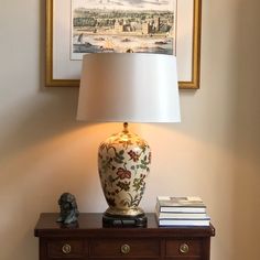 a lamp sitting on top of a wooden table next to a painting and a book