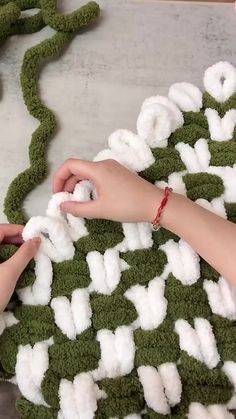 someone crocheting together yarn on top of green grass and another person is holding the yarn