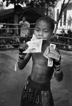 a black and white photo of a young boy eating food in front of a boxing ring