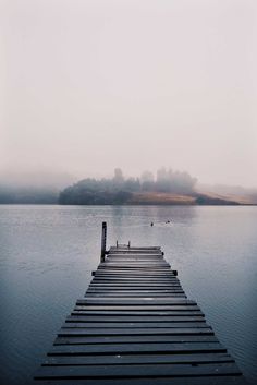 a dock sitting in the middle of a lake on top of a foggy day