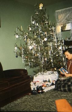 a woman sitting in front of a christmas tree with presents on the floor next to it