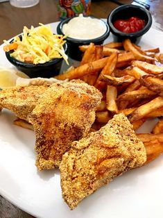 a white plate topped with fried chicken and french fries next to dipping sauces on the side