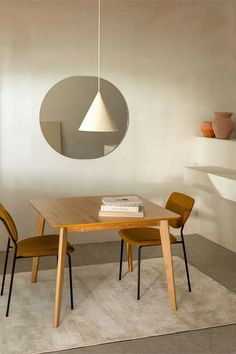 a wooden table with two chairs and a round mirror hanging from the wall above it