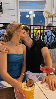 a man and woman sitting next to each other at a table with drinks in front of them