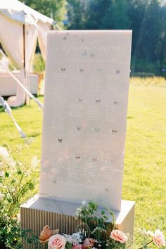 a wedding ceremony sign with flowers in the foreground and an open field behind it