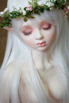 a close up of a doll with white hair and flowers on her head wearing a wreath