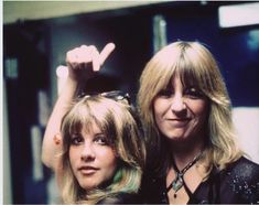 two women standing next to each other in front of a mirror with one pointing at the camera