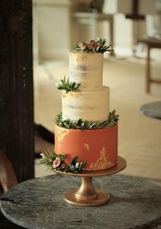 a three tiered cake with flowers and greenery on top sitting on a table