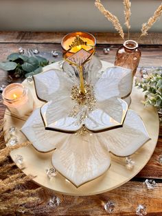 a white flower shaped plate with candles and flowers in it on top of a wooden table