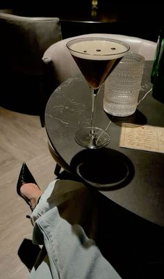 a martini glass sitting on top of a table next to a woman's legs