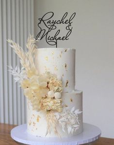 a three tiered wedding cake with flowers and leaves on the top is sitting on a wooden table