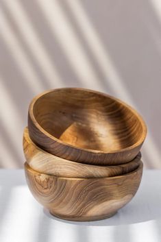 two wooden bowls sitting side by side on a white tablecloth with shadows from the wall behind them