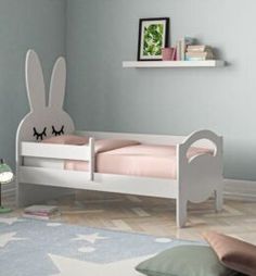 a white bed with pink sheets and bunny ears on the headboard is next to a book shelf