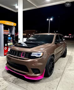 a brown jeep parked in front of a gas station at night with neon pink lights