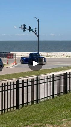 cars are driving down the road by the beach and ocean in front of a fenced off area