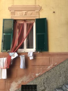 clothes hanging out to dry in front of an open window with green shutters and red drapes