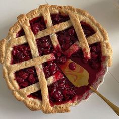 a cherry pie on a white table with a wooden serving utensil next to it