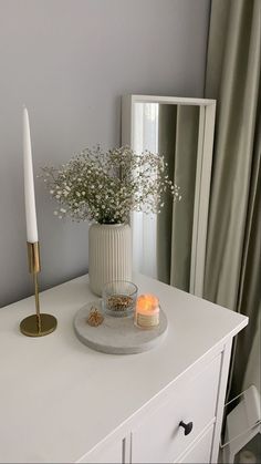 a vase with flowers and candles on a white dresser next to a mirror in a room