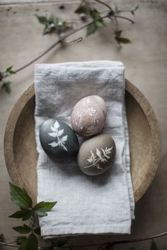 three painted rocks sitting on top of a white napkin next to green leaves and branches