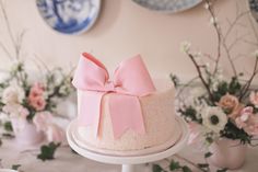 there is a cake with pink bows on it and flowers in vases behind it