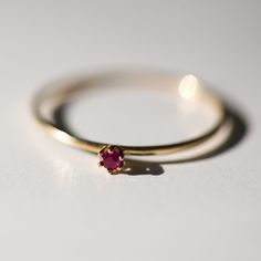 two gold rings with a pink stone on them sitting on a white surface, one has a tiny diamond in the middle