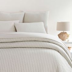 a bed with white comforter and pillows in a room next to a lamp on a table