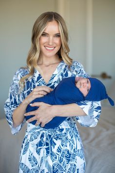 a woman holding a baby wrapped in a blue and white robe with palm leaves on it