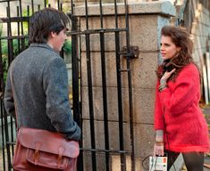 a man and woman standing next to each other in front of a gate with a handbag on it