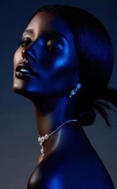 a woman with blue paint on her face and neck, posing for the camera in front of a dark background