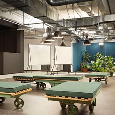 an empty room with green cots and plants in the center, surrounded by hanging lights