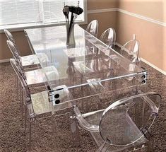 a glass dining table with clear chairs and flowers in vase on carpeted room floor