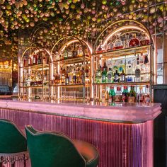 a bar with lots of bottles on the wall and green chairs in front of it