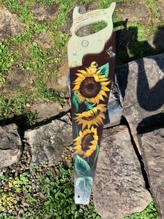 a pair of scissors with sunflowers painted on them sitting in the grass next to some rocks