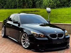 a black car parked in front of a green grassy area next to a brick walkway