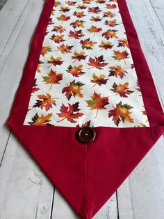 a red table runner with autumn leaves on it and a button in the center, sitting on a white wooden floor