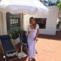 a woman in a white dress standing under an open umbrella on a brick patio area