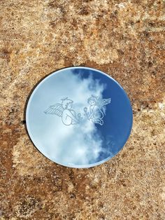 a round mirror sitting on top of a stone floor next to a blue sky and clouds