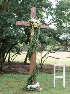 a wooden cross decorated with flowers and greenery in front of a white chair on the grass