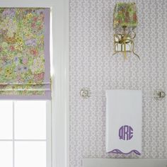 a bathroom with floral wallpaper and purple accessories on the shower curtain, toilet paper holder, and towel rack