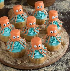 cupcakes with blue frosting and orange decorations on a wooden platter decorated with octopus heads