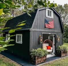 an american flag hangs on the side of a black barn with potted plants in front