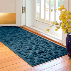 a blue door mat sitting on top of a wooden floor next to a vase with yellow flowers