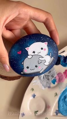 a hand holding a painted rock with two cats on it