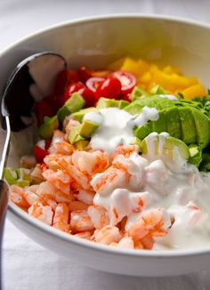 a bowl filled with shrimp, avocado, and sour cream dressing next to a spoon