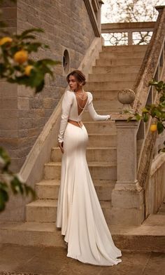 a woman in a long white dress standing on stairs with her back to the camera